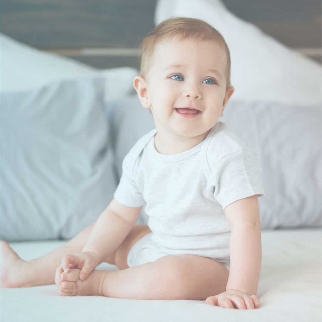 Bebê sentado na cama, sorrindo, ilustrando um novo salto do desenvolvimento